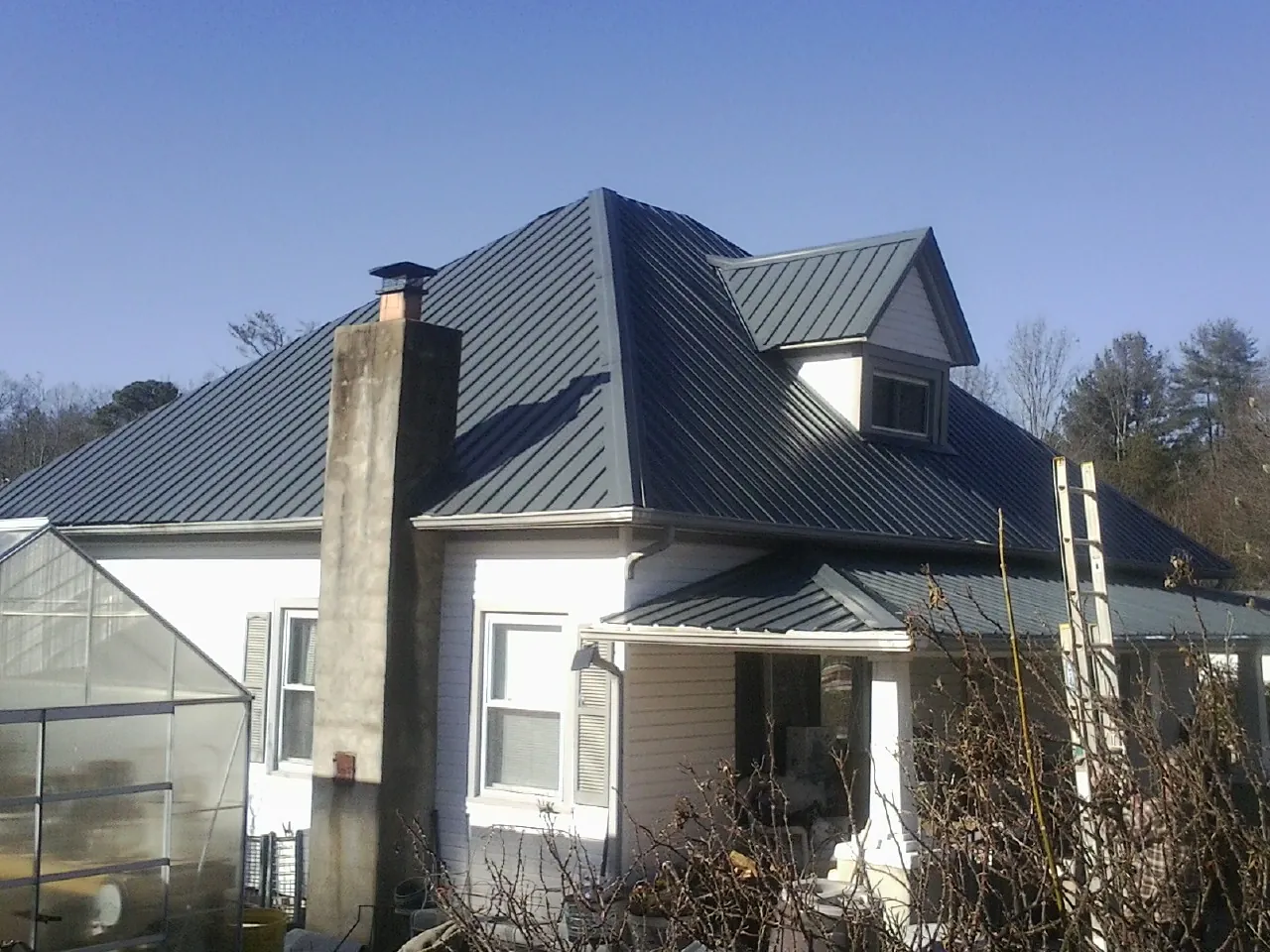 Dark blue standing seam metal roof on a white farmhouse with dormer — Slate & Tile Roof Repair by Roofing Brothers in Bevington