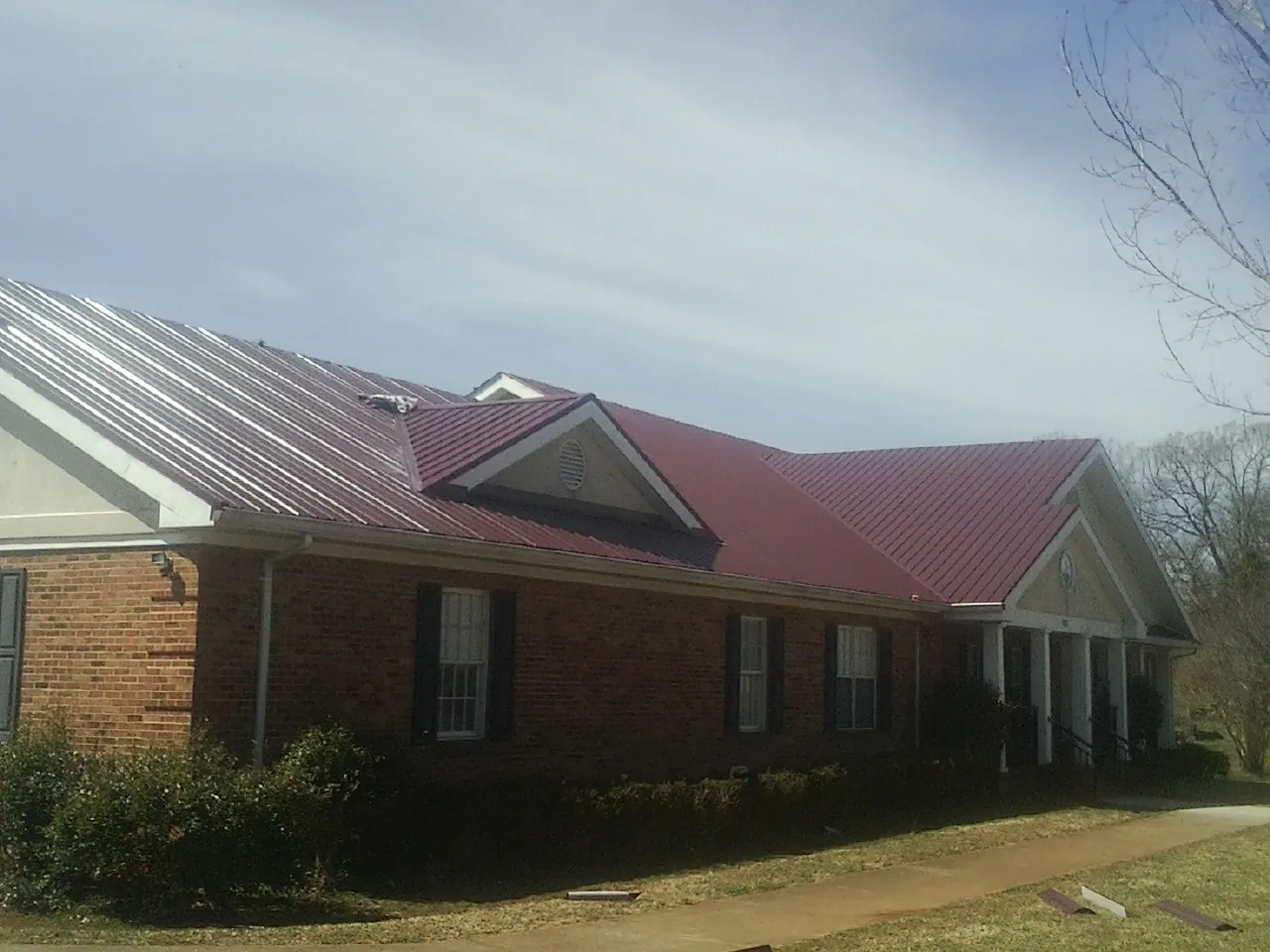 Red metal roof with gabled entries on a long brick building, from a Hail Damage Roof Repair job in Bevington