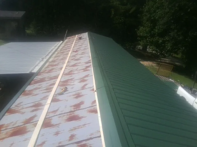 Old rusted panels beside newly installed green metal roofing — Wind Damage Roof Repair by Roofing Brothers in Bevington