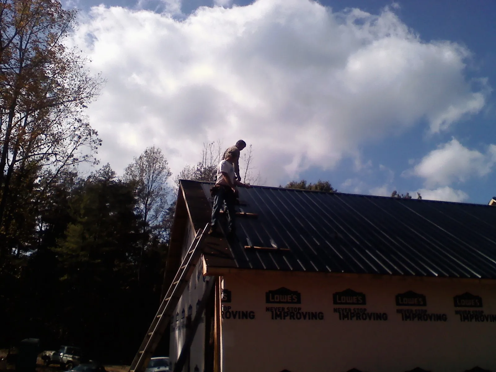 Roofer fastening dark metal panels high against a cloudy sky, from a Roof Inspection job in Bevington