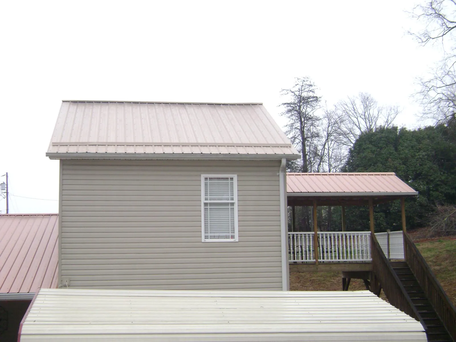 Tan metal roofs on a two story addition and attached porch, from a Roof Replacement job in Bevington